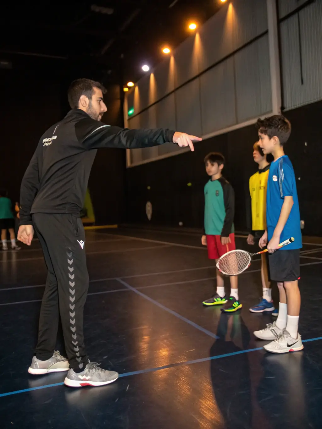 A focused shot of a table tennis training session at ETT, showcasing a coach guiding a player on proper form and technique, with other players practicing in the background.